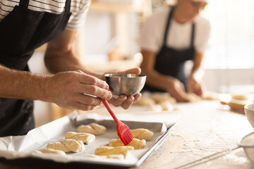 Baker's hands grease pieces of dough on baking sheet