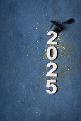 Graduation cap on wooden number 2025 on dark background. Class of 2025 concept
