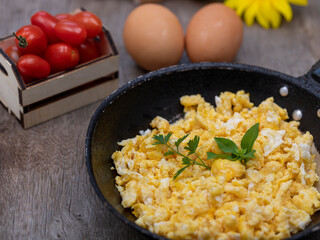 Scrambled eggs in an iron pan on the rustic wooden table