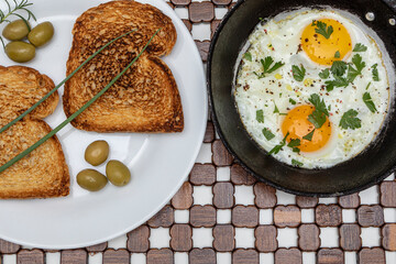 Fried eggs in a rustic iron pan, toast on a dish for breakfast. Top view