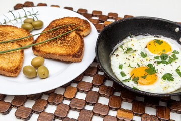 Fried eggs in a rustic iron pan, toast on a dish for breakfast