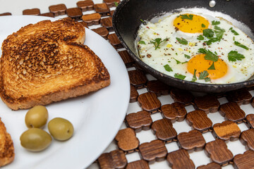 Fried eggs in a rustic iron pan, toast on a dish for breakfast