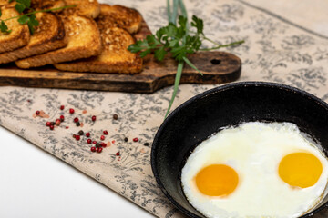 Fried eggs in a rustic iron pan, toast on a wooden board and a cup of coffee for breakfast.