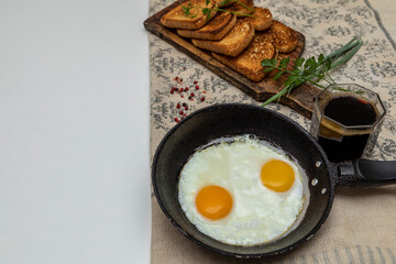 Fried eggs in a rustic iron pan, toast on a wooden board and a cup of coffee for breakfast.