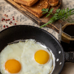 Fried eggs in a rustic iron pan, toast on a wooden board and a cup of coffee for breakfast.