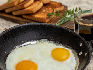 Fried eggs in a rustic iron pan, toast on a wooden board and a cup of coffee for breakfast.