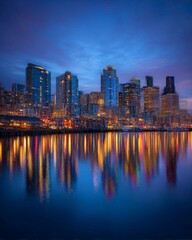 Fototapeta premium City skyline illuminated at dusk with reflections shimmering on the water, showcasing modern architecture and vibrant lights