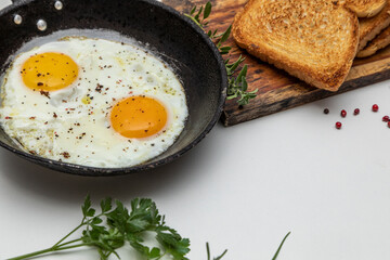 Fried eggs in a rustic iron pan, toast on a dish for breakfast