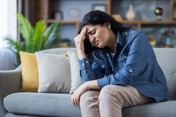 A woman is resting on a sofa with a headache, looking frustrated and stressed out.