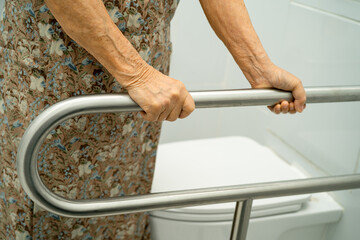 Asian elderly woman patient use toilet support rail in bathroom.
