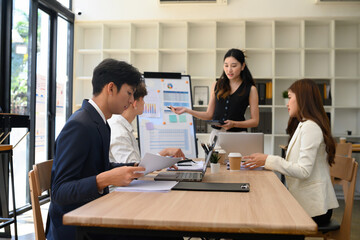 A team of young professionals attentively listens as a businesswoman leads a presentation in a modern office