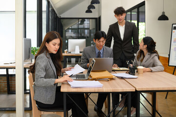 A Young professional businesswoman is engaged in focused work with laptops, documents, and conversation during a business meeting