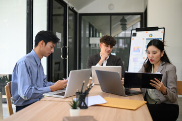 Three young professionals in a business meeting reviewing documents and working on laptops in a modern office