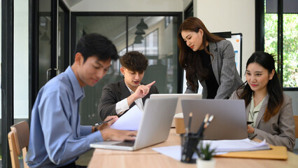 Fototapeta premium A group of young professionals collaborating on a business project. Team members review documents, use laptops, and engage in strategic planning in a bright, modern office setting