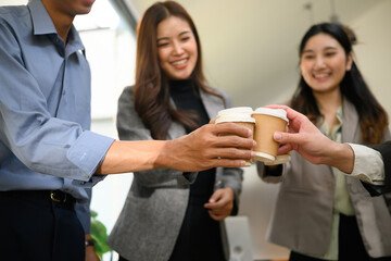 Close-up of diverse business team clinking coffee cups in celebration at a modern office. Smiling colleagues enjoy a casual and positive moment together