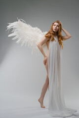 Red naked woman with angel wings and bodyart poses gracefully in studio setting