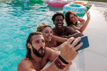 Friends taking photo of themselves in swimming pool during summer party