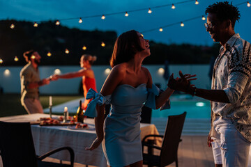 Friends enjoying dancing together at summer night party near swimming pool