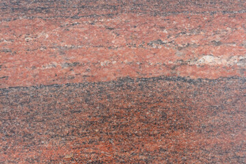 Close-up view of a rugged reddish granite stone surface showcasing unique natural patterns and textures. This stone features a diverse array of mineral inclusions, creating visual interest.