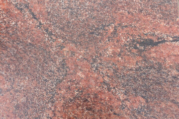 Close-up view of a rugged reddish granite stone surface showcasing unique natural patterns and textures. This stone features a diverse array of mineral inclusions, creating visual interest.
