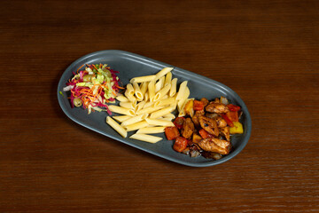 Chicken in sweet and sour sauce. Chicken wings in sweet and sour sauce on a plate with pasta and salad mix on a table in a restaurant
