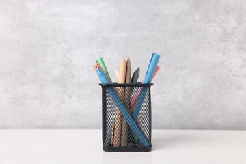 Ballpoint pens in holder on light wooden table against grey background