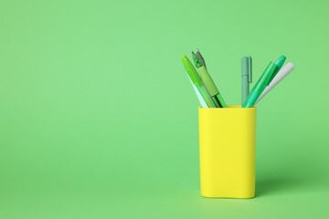 Ballpoint pens in holder on green background, closeup. Space for text