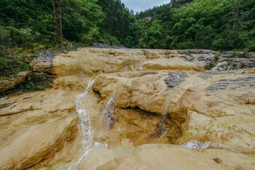 Cascading Water Over Rocky Terrain in a Lush Forest. Scenic view of water flowing and cascading over textured rocks in a green, forested environment. Pozas de San Martin