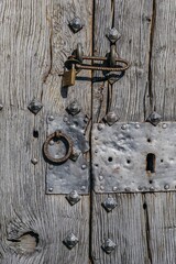 Ancient church door with decorative iron hardware in traditional stone archway. Historic wooden entrance with metal studs and keyhole set in rustic masonry wall with worn stone steps. Guaso, Huesca