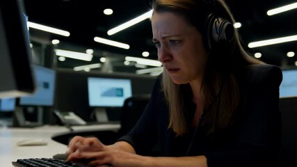 Focused professional crying female call centre operatore typing on computer in modern office at night
