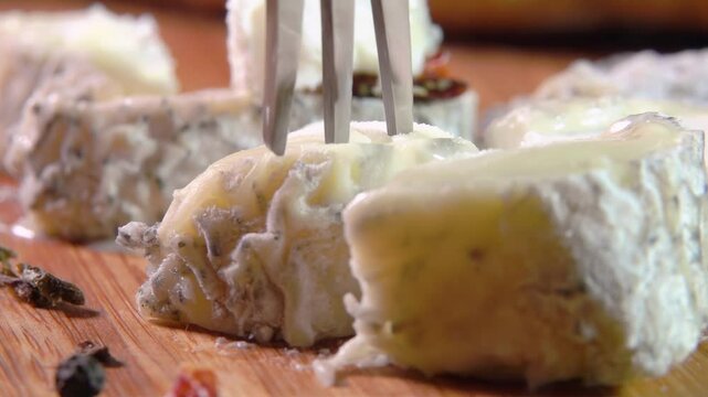 Fork breaks and raises a slice of goat cheese with gray mold from a wooden board. High quality 4k footage