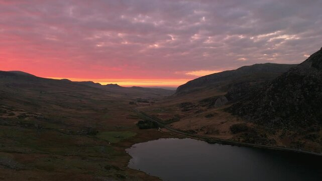 Llyn Ogwen lake with A5 road along the shoreline between mountains during sunrise with pink sky
