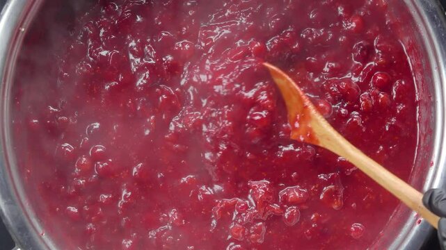 A wooden spoon stirs the boiling cranberry sauce, scoops it up and lifts it up. Top view. High quality 4k footage