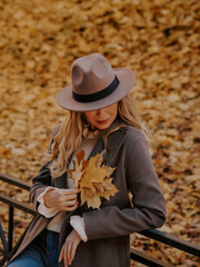 Beautiful blonde young woman in hat walking in autumn park. Her eyes are covered with a hat