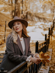 Beautiful blonde young woman in hat and coat walking on the stairs in the autumn park.