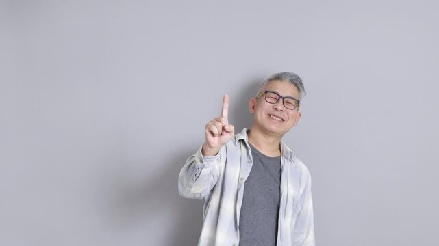 The senior East Asian man, wearing a white plaid-patterned shirt, is standing against a grey background.