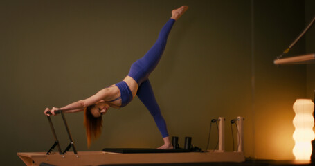 Woman doing pilates exercise on Pilates Reformer for the chest and back muscles, focusing on flexibility, strength, and control with determination