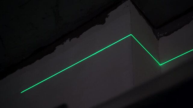 Unfinished walls and exposed beams surround the green laser level, creating sharp lines on the ceiling.