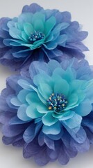 Obraz premium Two blue fabric flowers resting flat in studio lighting showcasing delicate petals and beaded centers