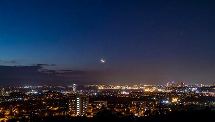 Night Cityscape Under Crescent Moon: A Panoramic View of Urban Lights and Celestial Beauty