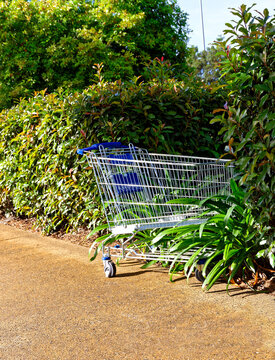 Abandoned blue shopping trolley on footpath and pushed into the hedge
