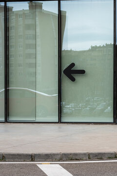 Glass door with black arrow symbol pointing left. Urban transparency and minimalist signage with visual contrast. Clean reflections, direction and public space orientation concept.