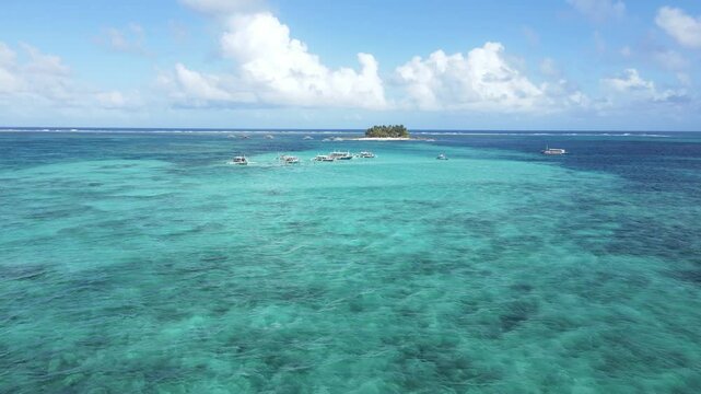 Drone approach to Guyam Island, Philippines. Crystal-clear turquoise waters, boats floating near the reef, and a small tropical paradise. Perfect for travel, adventure, and island-hopping