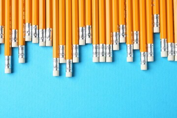 Pencils with erasers on light blue background, flat lay. Space for text