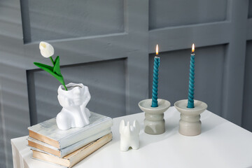 Candlesticks with burning candles on table near grey wall