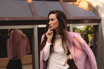 Young brunette long hair woman standing with doubt expression at street, girl wear pink blazer, think about something, arm on chin.