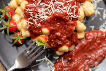 Close up on fork with gnocchi and plate of gnocchi with blurred red sauce in the background