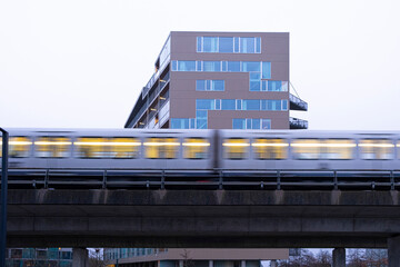 Yellow train in motion crossing through Copenhagen’s Ørestad district. Urban mobility, speed, infrastructure and geometric city backdrop in architectural cityscape concept.
