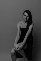 Naklejka premium A slim, beautiful Caucasian woman in a black dress, brunette, against a peach background, with glowing skin and a smile.