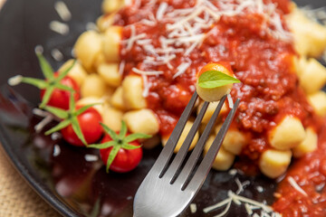 Close up on fork with gnocchi and plate of gnocchi with blurred red sauce in the background